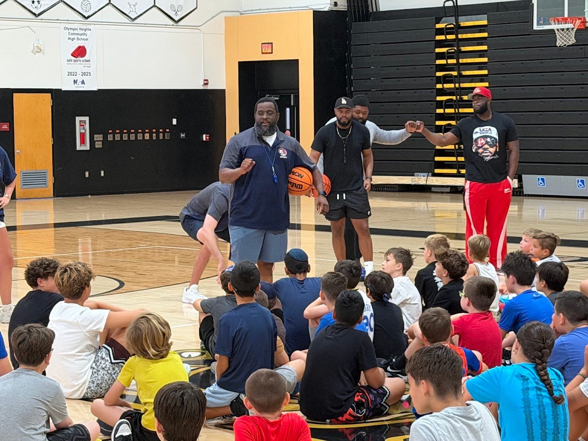 Boca Basketball summer camp coaches demonstrating to seated campers at Olympic Heights High School